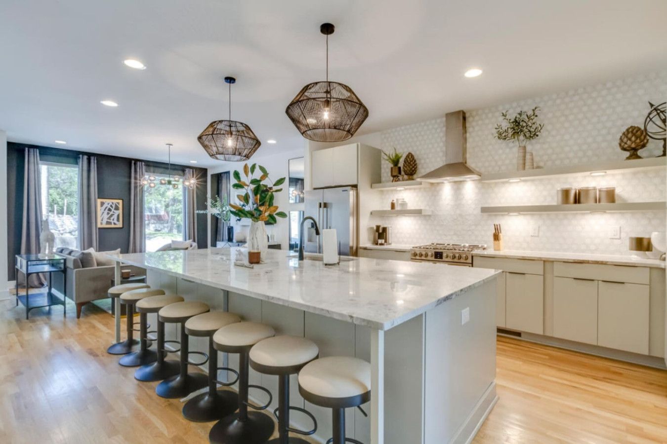 A modern kitchen with a large island, bar stools, pendant lighting, and a view of the outdoors.