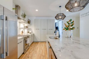 A modern kitchen with white cabinetry, a marble countertop, and a wooden floor. - Last Call Lounge & Midtown Skyline | 2 Homes (Nashville)