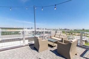 A rooftop terrace with wicker furniture, a view of the city skyline, and a swimming pool in the background. - Last Call Lounge & Midtown Skyline | 2 Homes (Nashville)