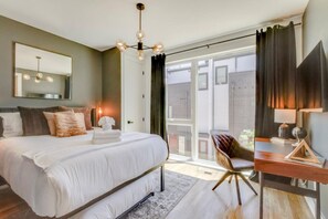 Een moderne slaapkamer met een groot bed, een bureau en een stoel. Er is een groot raam met gordijnen en uitzicht op buiten.