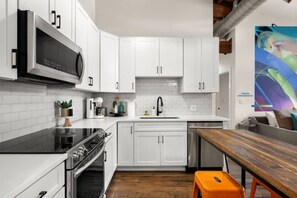 A modern kitchen with white cabinets, a black stove, and a wooden dining table. - Suite and Speakeasy | Pool + Mins to Broadway (Nashville)