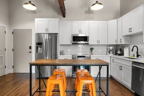 A modern kitchen with white cabinets, stainless steel appliances, and a wooden island with orange stools. - Suite and Speakeasy | Pool + Mins to Broadway (Nashville)