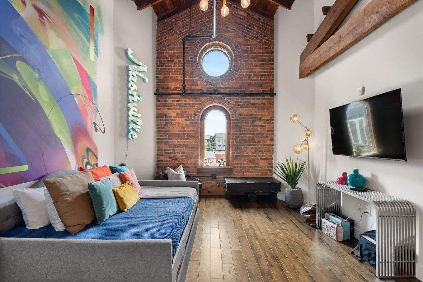 Een gezellige kamer met een bed, een televisie, een bakstenen muur en een dakraam.