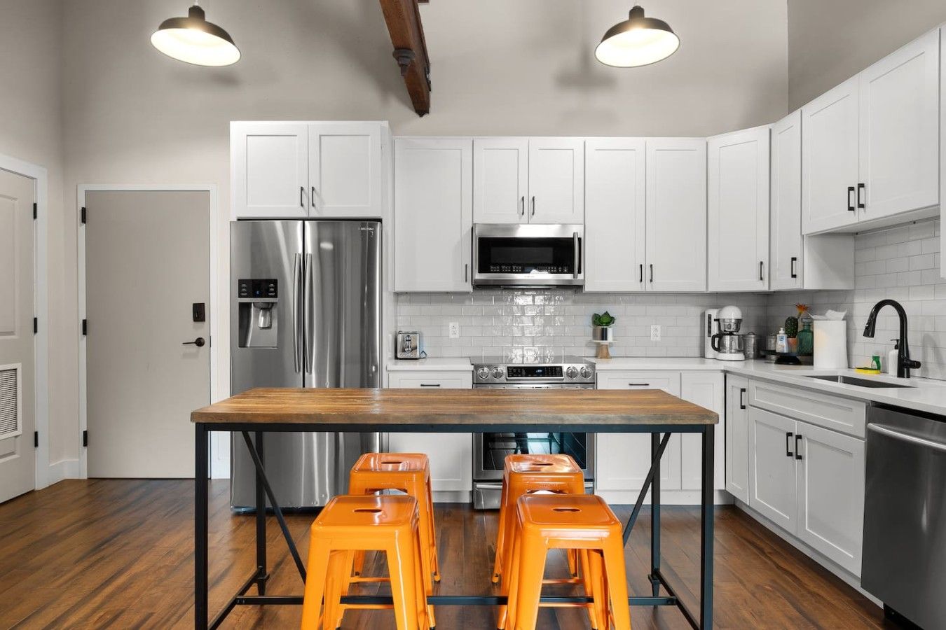 A modern kitchen with white cabinets, stainless steel appliances, a wooden island with stools, and pendant lighting.