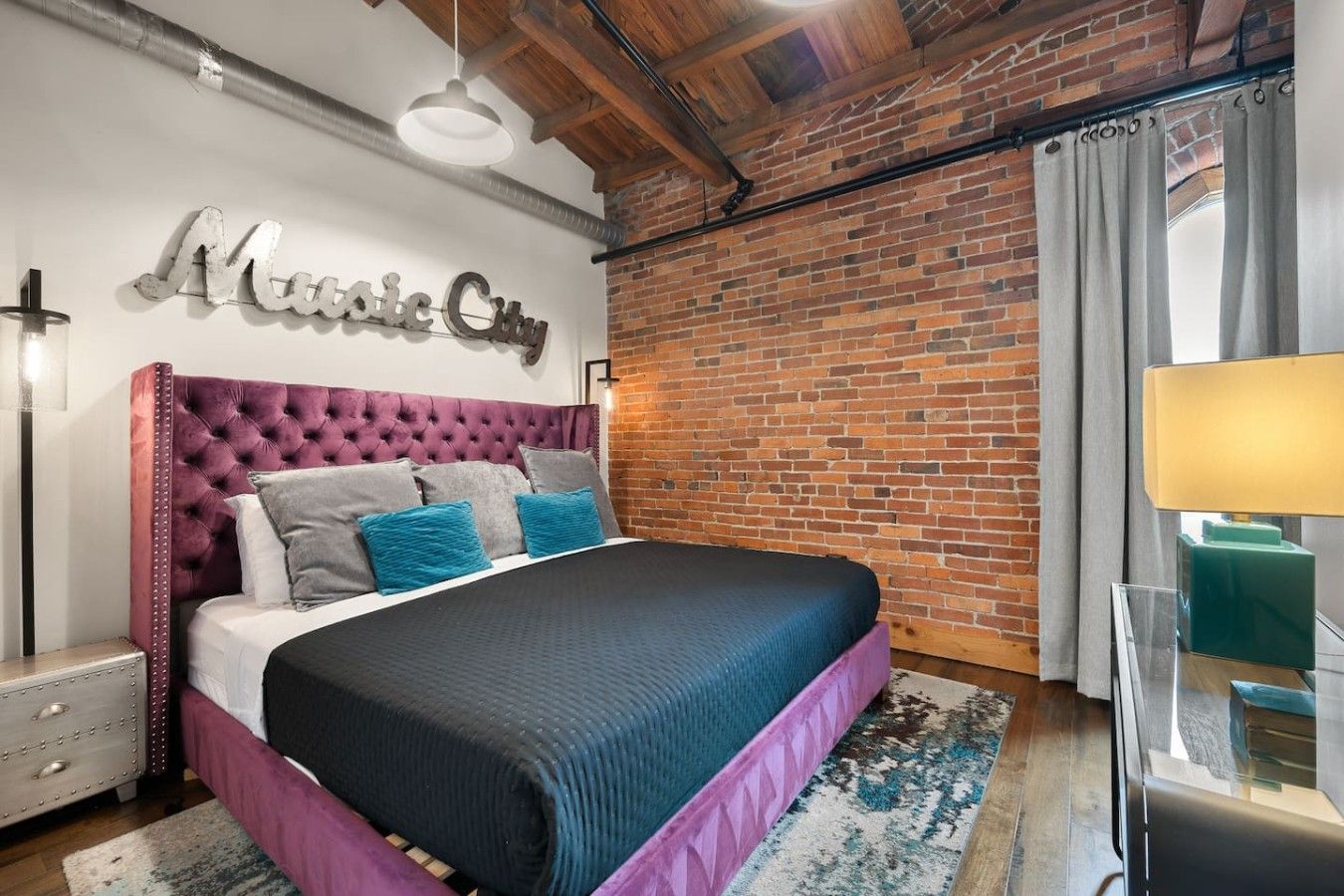 A bedroom with a brick wall, a bed with a tufted headboard, and a sign that reads 'Music City'.