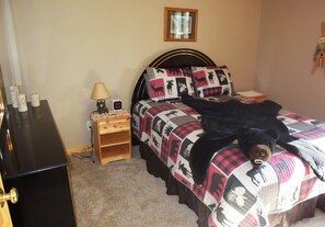 A bedroom with a bed, a nightstand, a lamp, and a dresser.