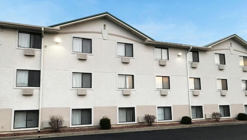 A multi-story hotel with a flat facade, air conditioning units, and a parking lot in front.