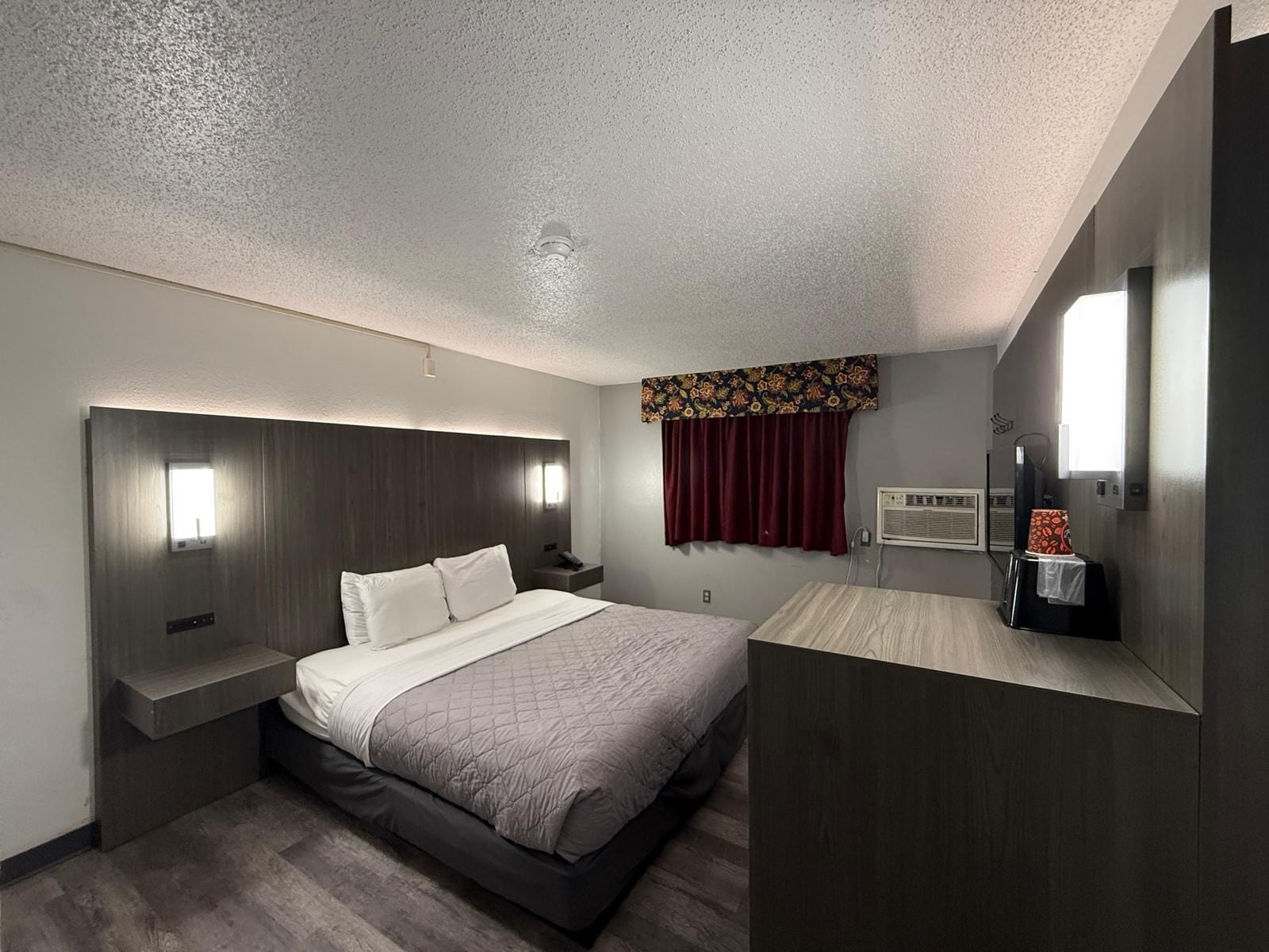 Habitación de hotel moderna con una cama grande, una mesita de noche, televisión integrada y ventana con cortinas.