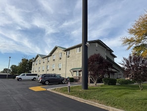 Un hotel de varios pisos con estacionamiento, un área verde y cielo despejado.