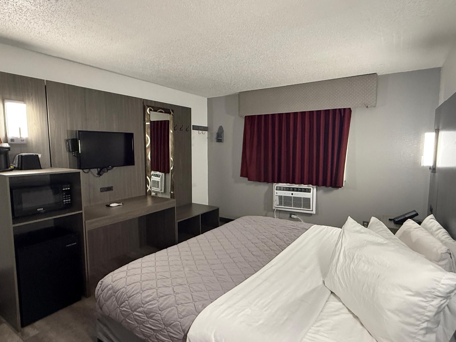Habitación de hotel con cama, escritorio con computadora, televisor y ventana con cortinas.