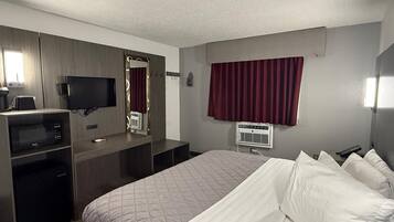 Habitación de hotel con cama, escritorio con computadora, televisor y ventana con cortinas.