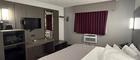 Habitación de hotel con cama, escritorio con computadora, televisor y ventana con cortinas.