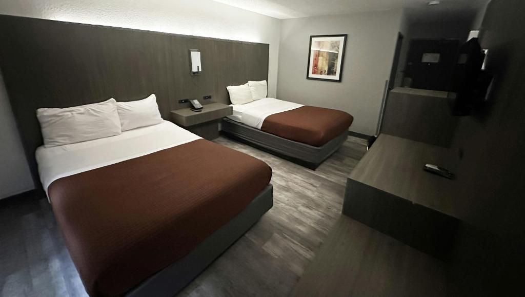 A hotel room with two beds, a desk, a phone, and a framed picture on the wall.