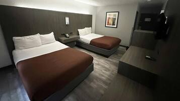 A hotel room with two beds, a desk, a phone, and a framed picture on the wall.
