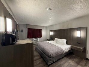 Habitación de hotel con cama, mesitas de noche, escritorio con cafetera, ventana con cortinas y aire acondicionado de pared.