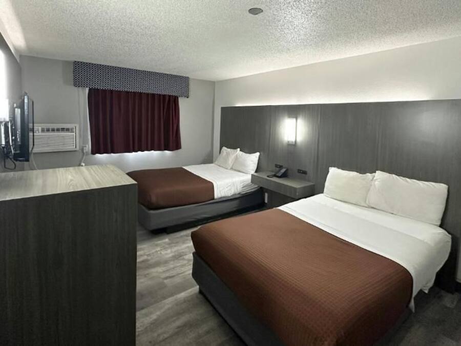 Une chambre d’hôtel avec deux lits, un bureau, une chaise, une télévision et une fenêtre avec des rideaux.