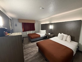 Habitación de hotel con dos camas, un escritorio, cafetera, ventana con cortinas y una lámpara de pared.