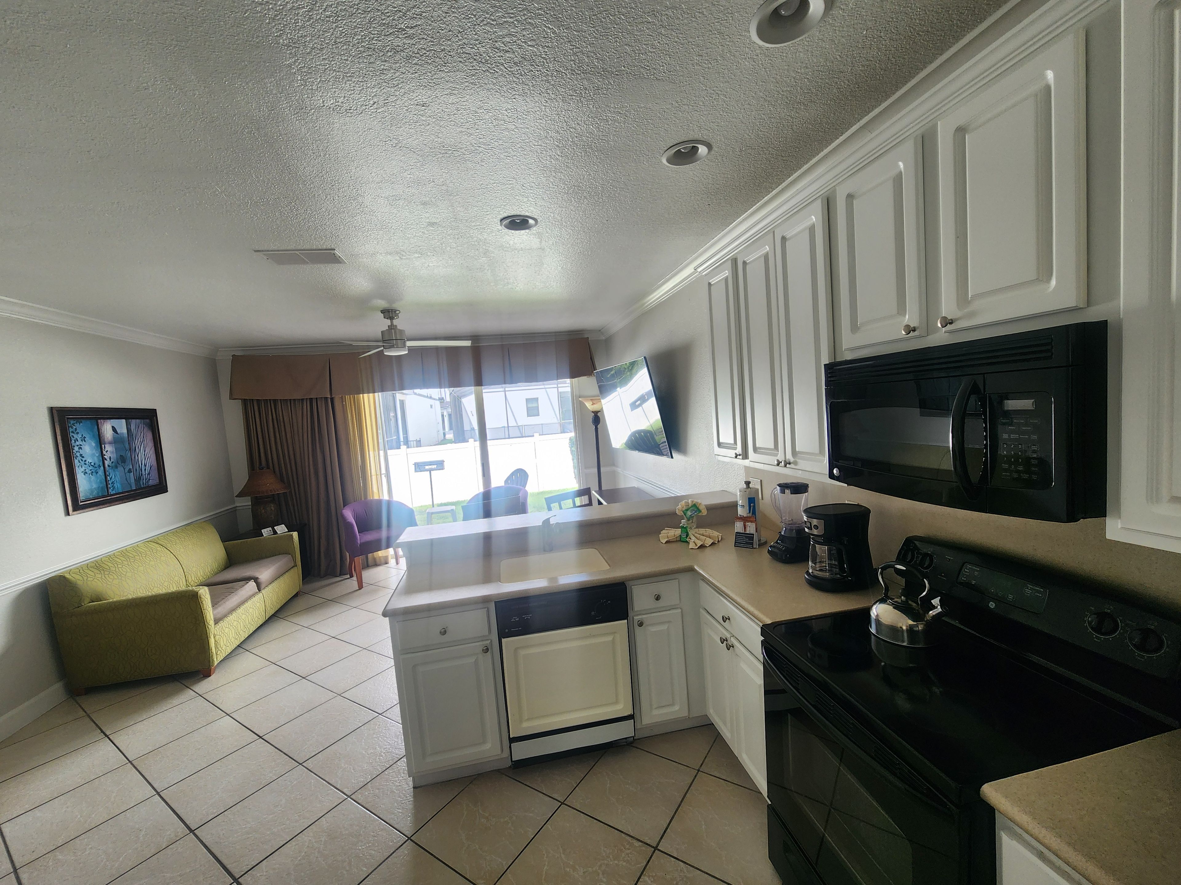 A compact kitchen with white cabinetry, a black microwave, a coffee maker, and a dishwasher.