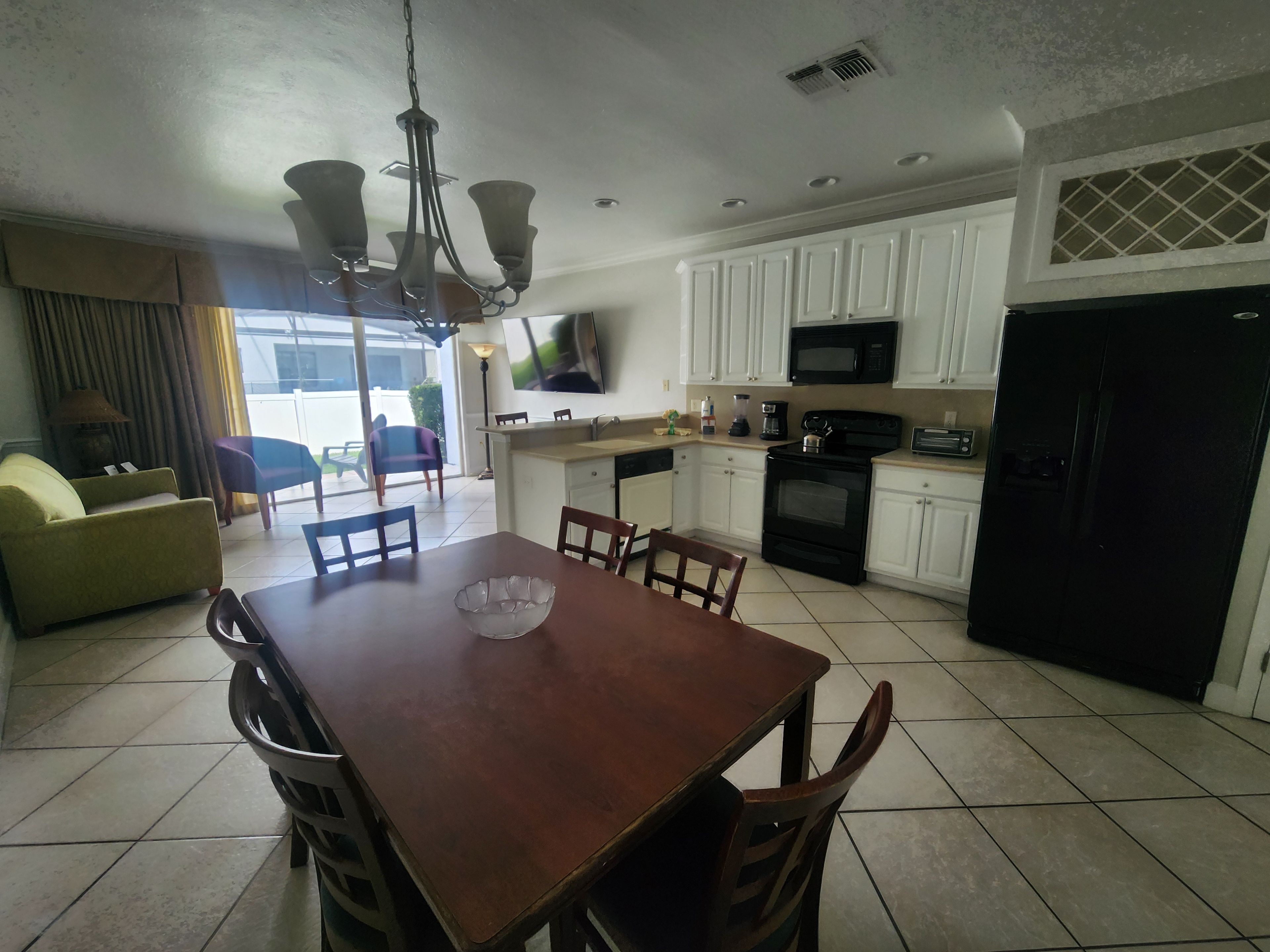 A modern kitchen with white cabinets, a black refrigerator, and a dining area with a wooden table and chairs.
