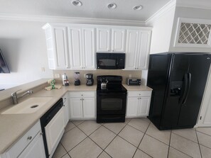 A kitchen with white cabinets, a black refrigerator, a microwave, a toaster, and a stove. - Tranquil 2-bedroom townhome by SeaWorld 4 (Orlando)