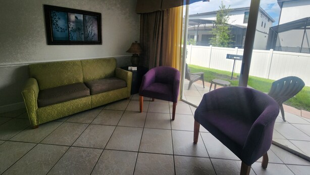 Een woonkamer met een bank, twee fauteuils, een lamp en een schilderij aan de muur.
