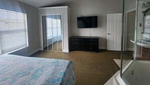 Een slaapkamer met een bed, een dressoir, een televisie en een plafondventilator.
