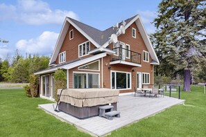 Une maison à deux étages dotée d’une terrasse, d’un espace extérieur aménagé et couvert, et d’une grande fenêtre.