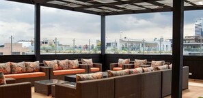 Eine Dachterrasse mit Korbmöbeln und orangefarbenen Kissen, die einen Blick auf die Stadt bietet.