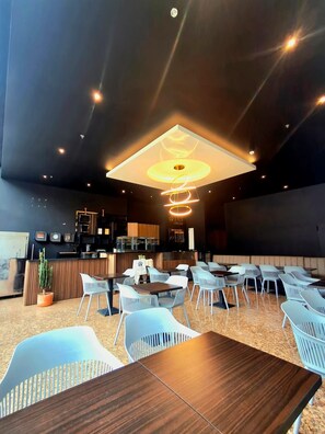 Een modern restaurantinterieur met een centrale bar, een zithoek en een opvallende plafondlamp.
