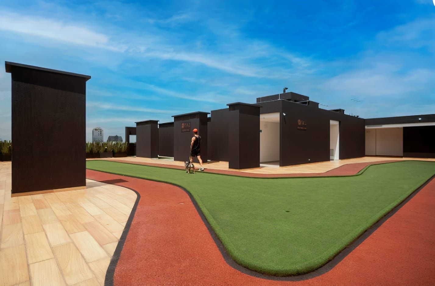 Un edificio moderno con techo plano, un área pavimentada con césped artificial y una persona caminando.
