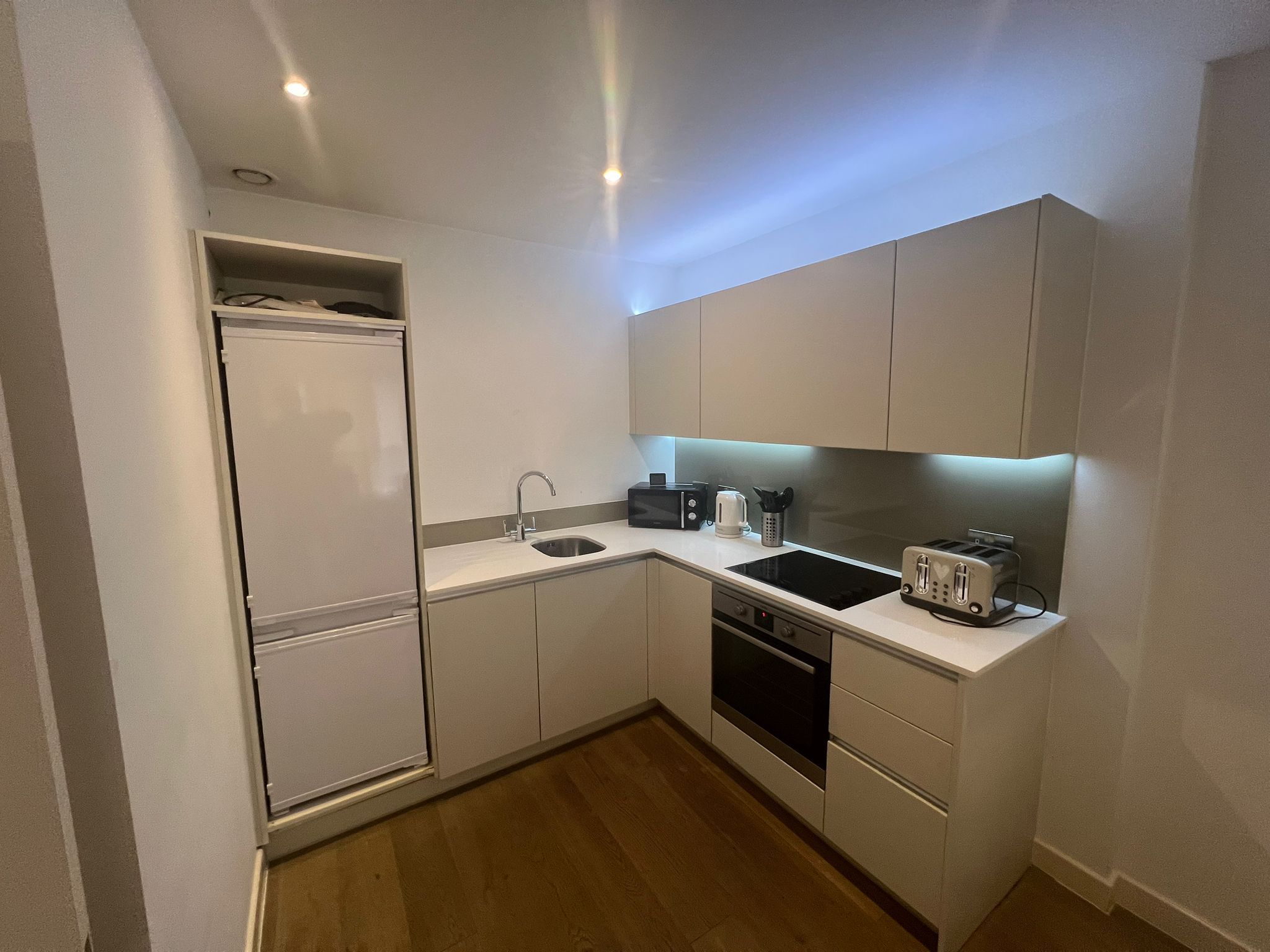 A compact kitchen with a refrigerator, sink, microwave, toaster, and a dishwasher.