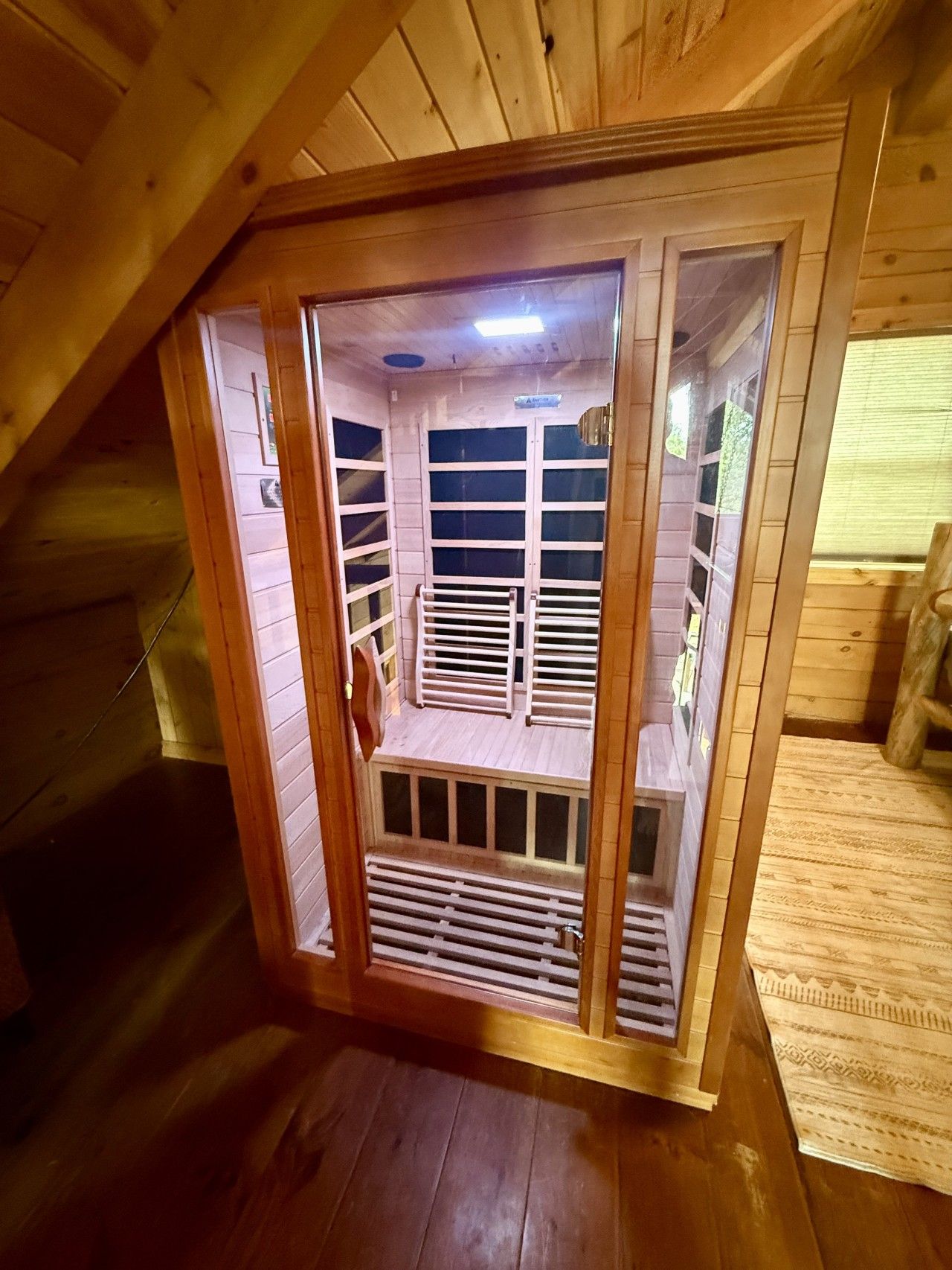 A wooden attic room with a sloped ceiling, a built-in window, and a wooden door.