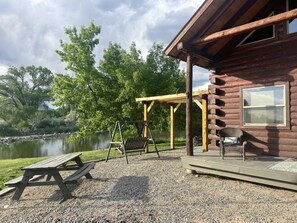 Una cabaña de madera con una mesa de picnic y un columpio junto a un lago.