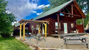 Een rustieke hut met een overdekte veranda, een schommel en een picknickplaats.