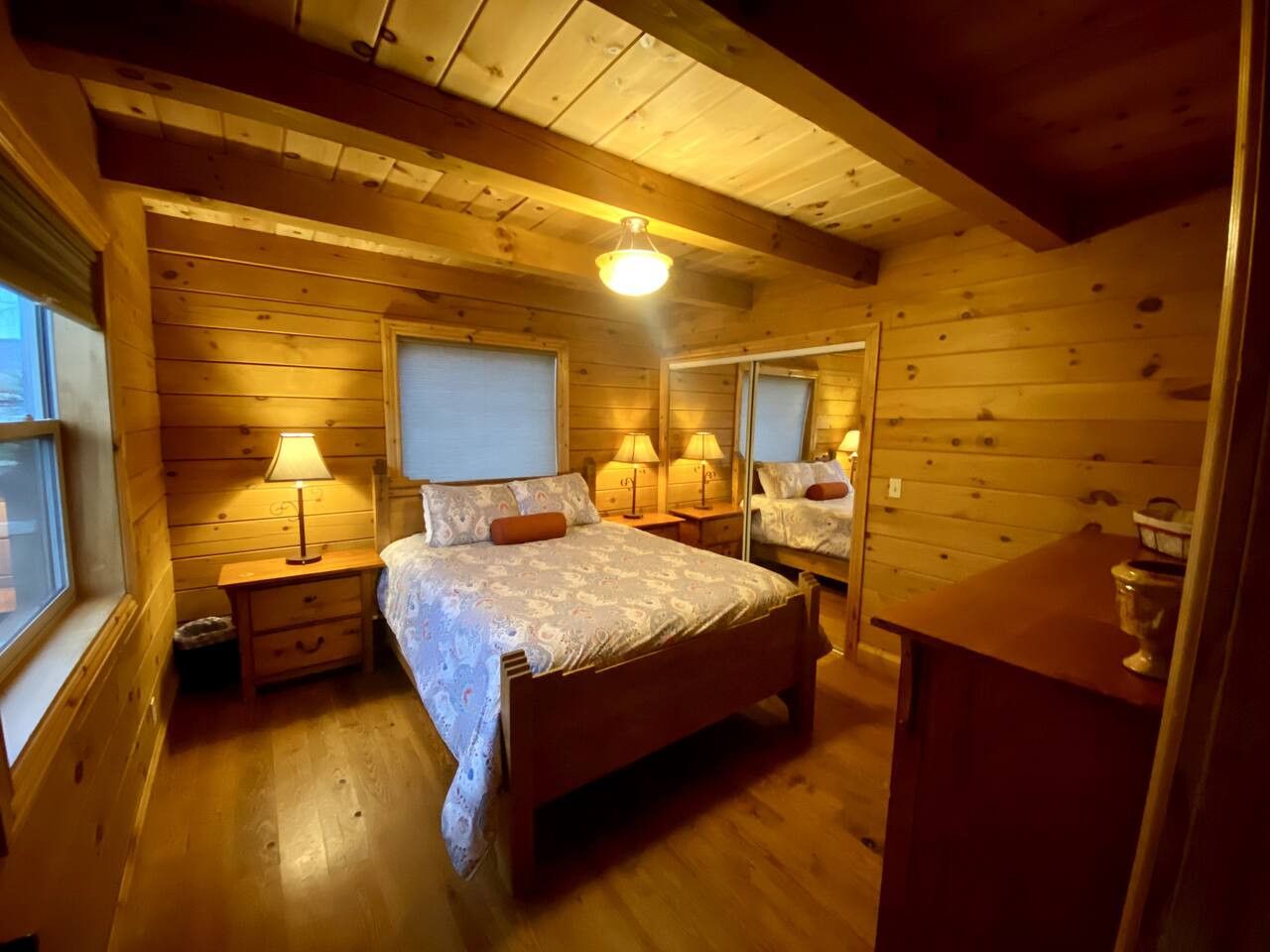 Ein Schlafzimmer einer Holzhütte mit einem Bett, Nachttischlampen, einem Nachttisch und einer Kommode.