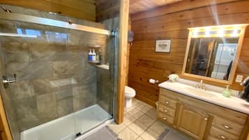 A bathroom with a glass-enclosed shower, a toilet, wooden cabinets, and a vanity with a mirror.