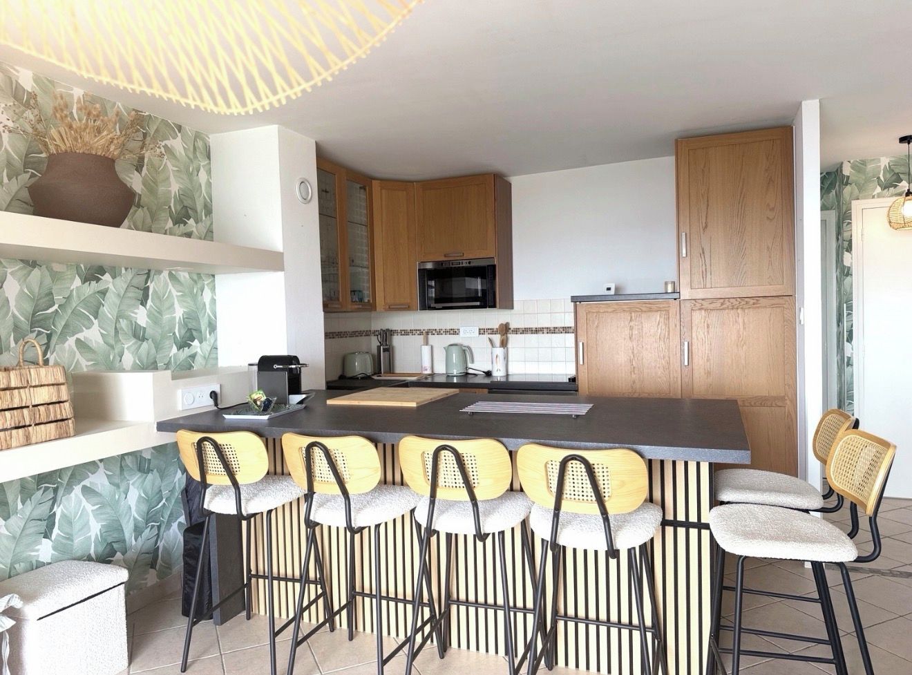 A modern kitchen with a central island, bar stools, wooden cabinets, and a microwave.