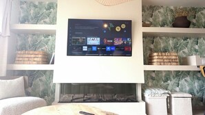 Un salon doté d’un téléviseur à écran plat fixé au mur, d’une cheminée et d’étagères ornées d’objets décoratifs.