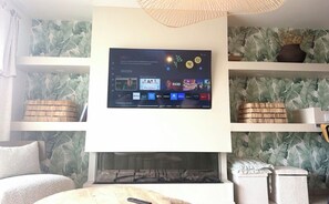 Un saló amb televisió plana penjada a la paret, una llar de foc i prestatges decorats amb objectes decoratius.