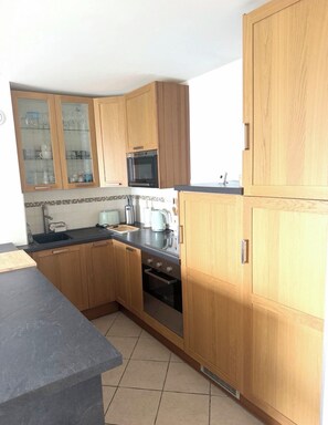 A kitchen with wooden cabinets, a microwave, a stove, and a sink. - A gem right by the sea 🌊 the Le Panoramic residence in Sainte-Cécile. (Camiers)