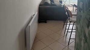 Une pièce avec un radiateur, un canapé, un fauteuil et une vue sur la mer par une fenêtre ornée de rideaux.