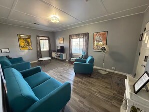Ein Wohnzimmer mit türkisfarbenen Sofas, einem kleinen Tisch, einem Fernseher und einer Stehlampe.