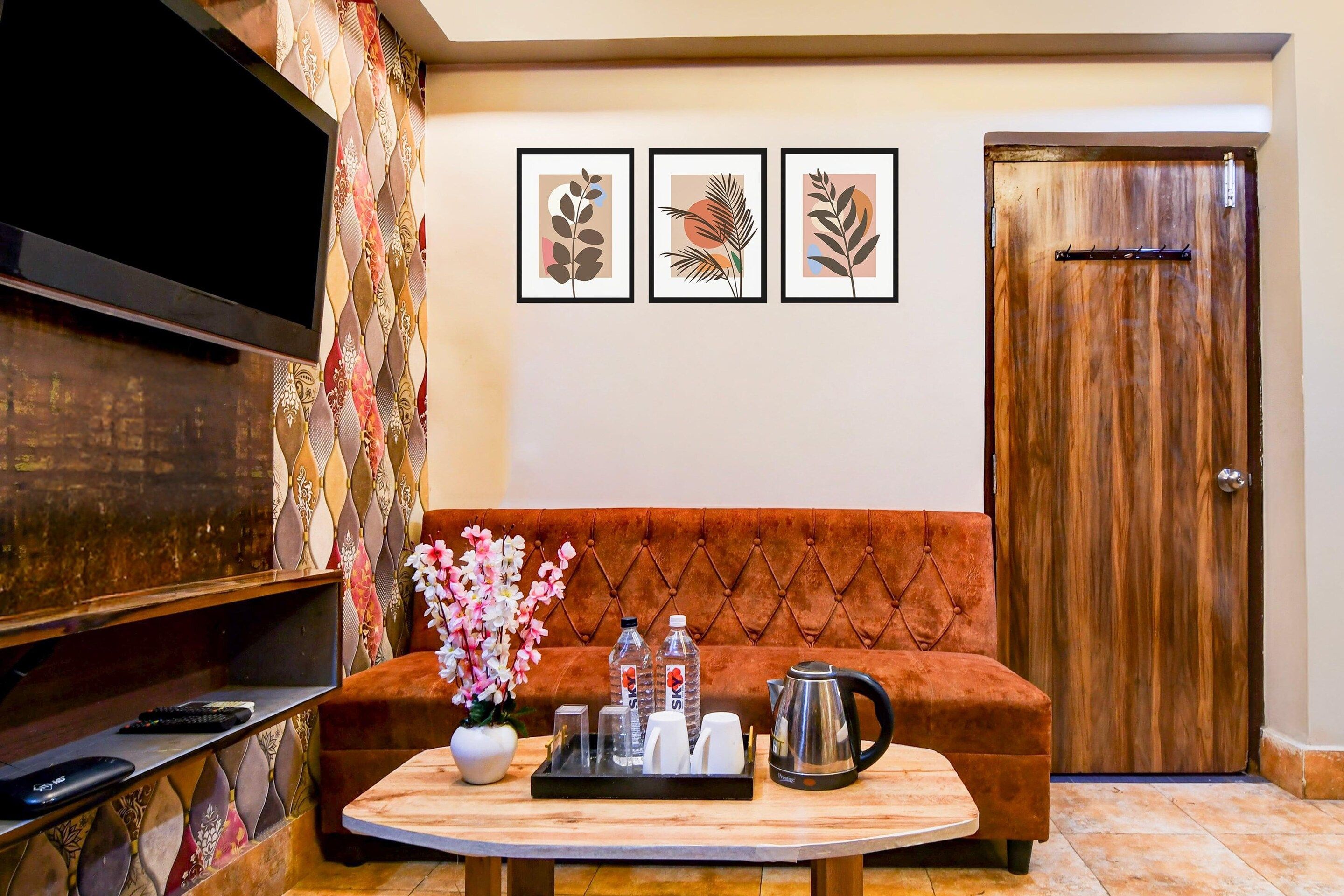 A living room with a flat-screen TV, a sofa, a coffee table with a tray of items, and framed artwork on the wall.