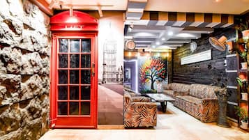 Una cabina telefónica roja, un sofá estampado con diseño de cebra, y una pared con un reloj y un cuadro enmarcado.