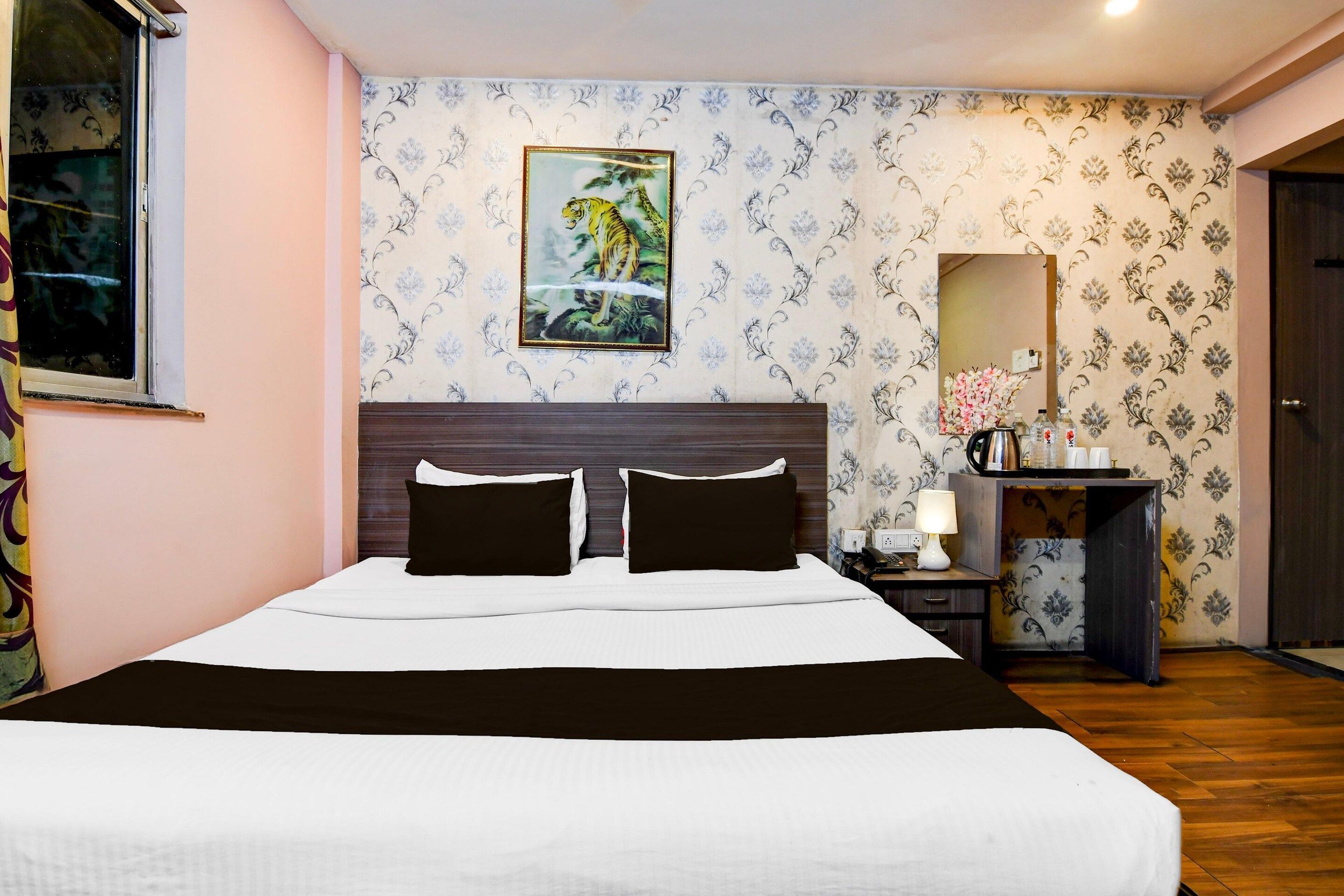 Habitación de hotel con una cama grande, una mesita de noche con lámpara, un espejo y un cuadro en la pared.