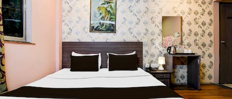 Habitación de hotel con una cama grande, una mesita de noche con lámpara, un espejo y un cuadro en la pared.