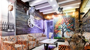 Ein Zimmer mit einem zebramusterten Sofa, einem Ventilator, einem Tisch mit einer Vase und einer farbenfrohen Baum-Mural.