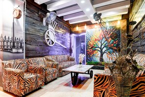 A room with a zebra-striped sofa, a fan, a table with a vase, and a colorful tree mural. - Super Collection O Circus Avenue Road (Kolkata)