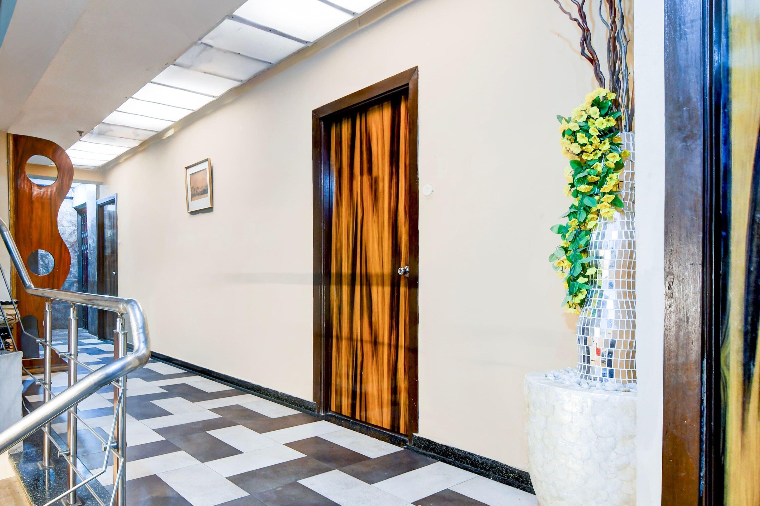 A hallway with a patterned floor, a wooden door, a metal railing, and a decorative plant.