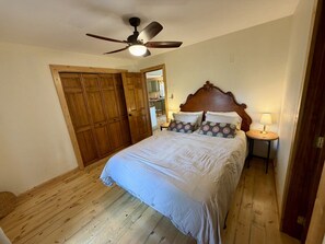 Ein Schlafzimmer mit einem Bett, Holzboden, Deckenventilator, Holzschrank und Nachttisch mit Lampe.